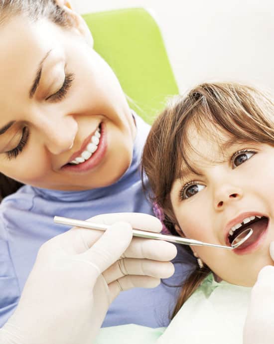 Pediatric dentist examining young child's teeth during routine dental checkup in clinical setting.