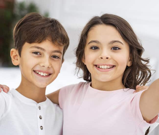 Two smiling children posing together outdoors for dental care website portrait.