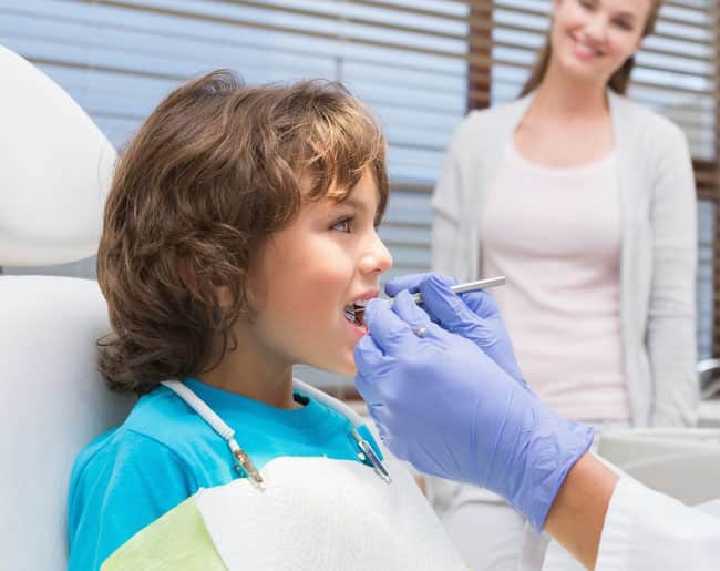 Child receiving dental examination from dentist wearing blue gloves in clinical office setting.