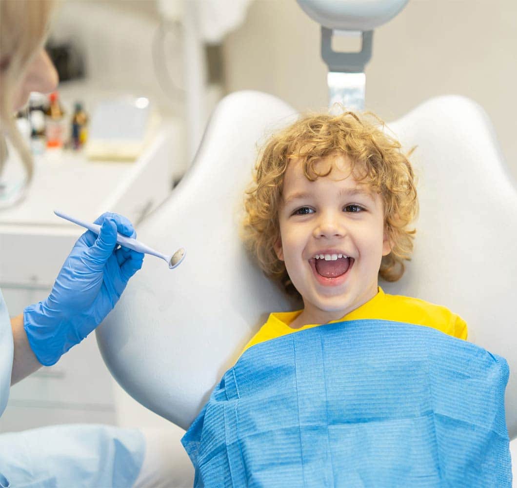 Happy young child in dental bib smiling at dentist appointment with tools visible.