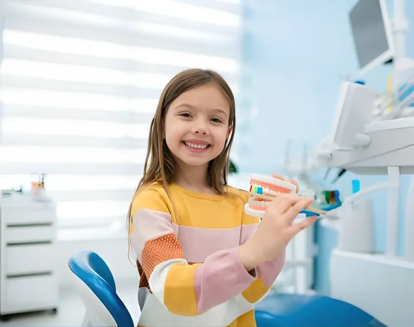 Young girl in yellow shirt holding toothbrush in modern dental office setting.